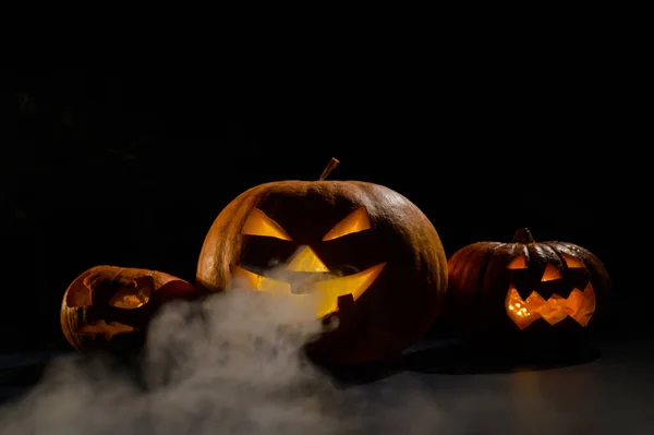 Calabazas con muecas talladas y velas en el interior en la oscuridad para Halloween. Jack o latern en el humo. —  Fotos de Stock