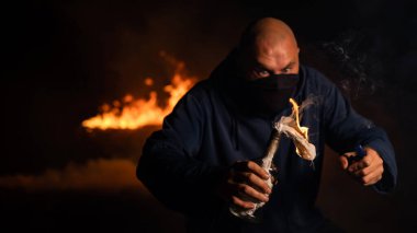 Maskeli bir adam yanan bir şişe tutuyor. Molotof kokteyli.