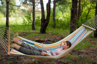 Ormandaki bir hamakta otururken dizüstü bilgisayarda çalışan beyaz bir kadın. Yürüyüşte kablosuz bilgisayar kullanan bir kız..