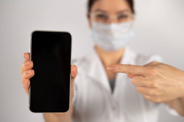 Doktor elinde beyaz arka planda siyah ekranlı bir akıllı telefon tutuyor..