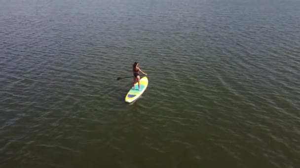Mujer caucásica montando una tabla SUP en el lago. Vista desde arriba. Deportes de verano. — Vídeos de Stock