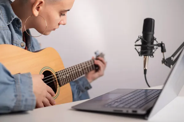 Junge kaukasische Frau mit kurzen blonden Haaren spielt Gitarre und streamt live auf Laptop. — Stockfoto