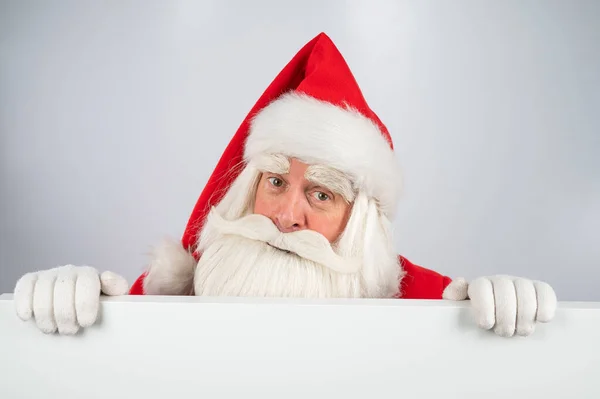Ο Άγιος Βασίλης κρυφοκοιτάζει πίσω από μια διαφήμιση σε λευκό φόντο. Καλά Χριστούγεννα.. — Φωτογραφία Αρχείου
