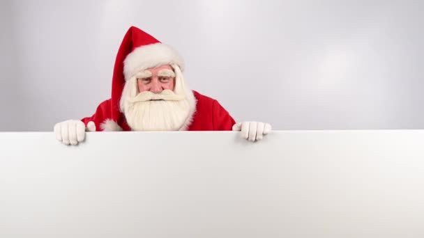 Papai Noel espreita por trás de um anúncio em um fundo branco. Feliz Natal!. — Vídeo de Stock