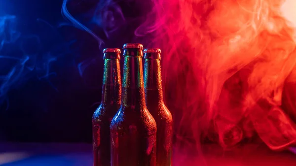 Três garrafas de cerveja em uma névoa azul-rosa. — Fotografia de Stock