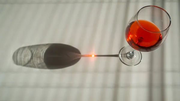 Um copo de vinho tinto em uma mesa branca com uma sombra das cortinas — Fotografia de Stock