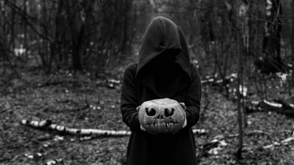 A witch holds a creepy pumpkin in a dense autumn forest. Jack o lantern for halloween. Monochrome — Stock Photo, Image