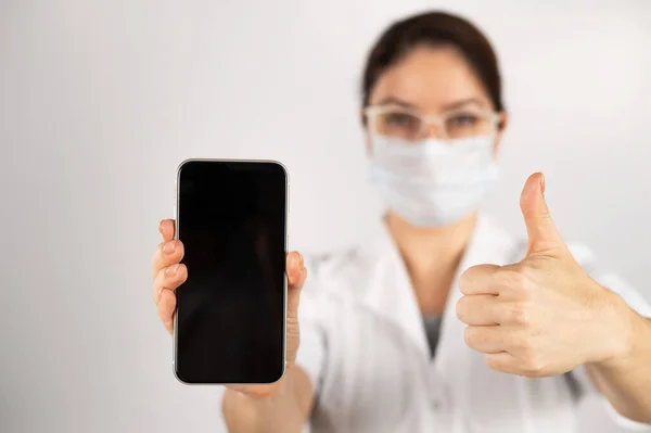 O médico segura um smartphone com uma tela preta em um fundo branco. — Fotografia de Stock