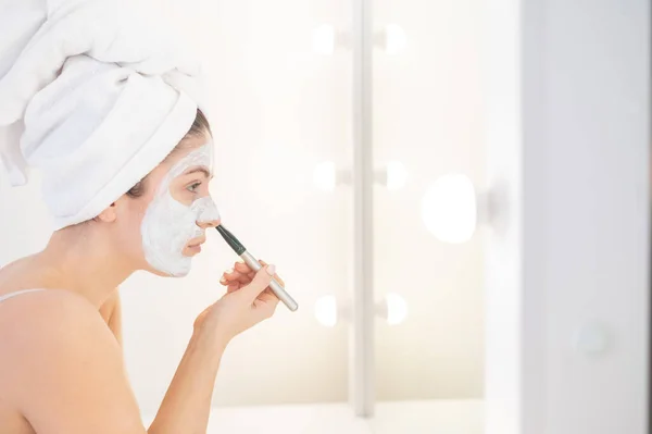 Mujer alegre con una toalla en el pelo y en una mascarilla de barro jugando con pepinos en las manos. Cuidar de la belleza en casa — Foto de Stock