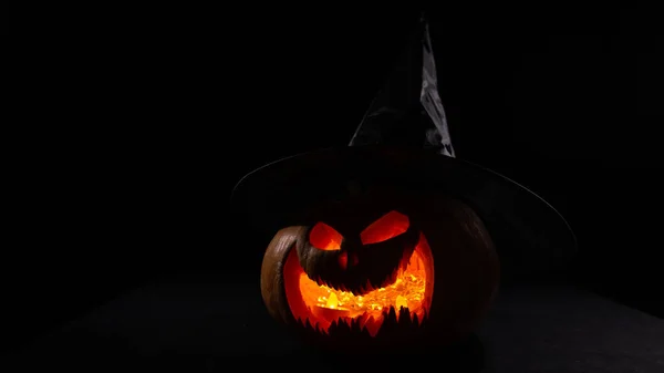 Gloeiende pompoen in een heksenhoed in het donker. Jack o lantaarn. — Stockfoto