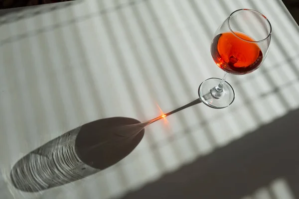 ブラインドから日陰のある白いテーブルの上に赤ワインのガラス — ストック写真