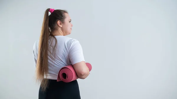 年轻的肥胖的高加索女人拿着一个运动垫。白底运动服的迷人+尺寸模型 — 图库照片