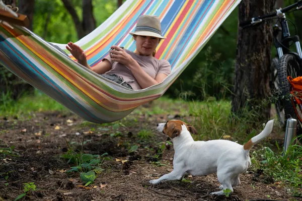 Donna caucasica si trova su un'amaca con Jack Russell Terrier cane in una pineta — Foto Stock