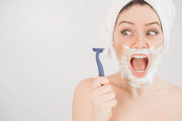 Funny portrait of a woman with shaving foam on her face holding a razor on a white background. The girl removes the mustache and beard — Stock Photo, Image