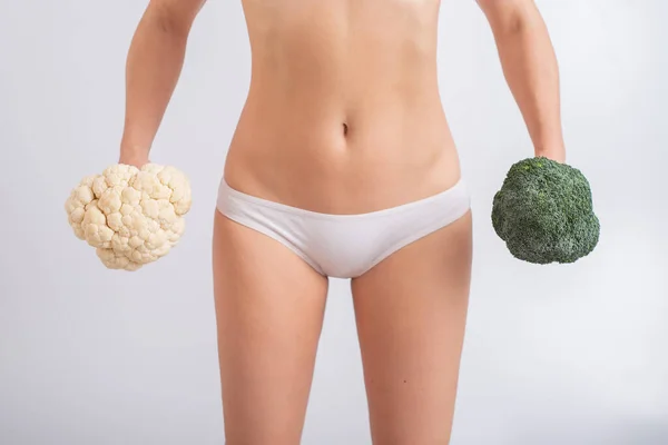 En ansiktslös kvinna i trosor håller blomkål och broccoli på en vit bakgrund. Matvanor. — Stockfoto