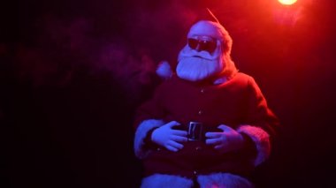 Mavi-kırmızı dumanın arasında güneş gözlüklü Noel Baba. Mutlu Noeller..