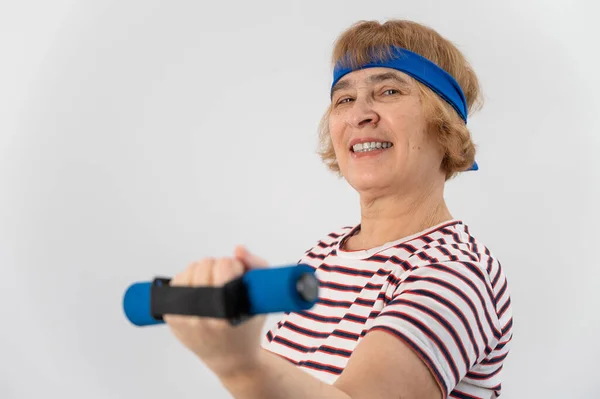 Šťastná stará žena dělá fitness cvičení s činkami na bílém pozadí. Starší dáma dělá fitness pro udržení zdraví. — Stock fotografie