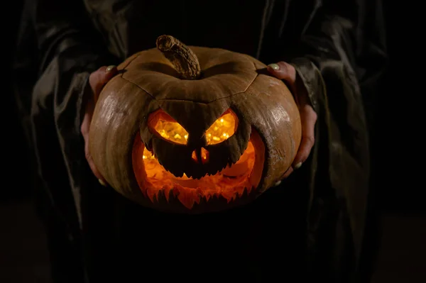 La strega sta tenendo una zucca jack o lanterna incandescente al buio. Halloween. — Foto Stock