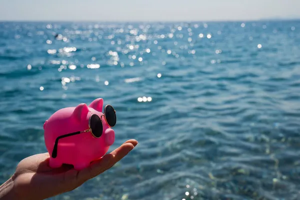 En kvinna håller en spargris i solglasögon på havets botten. Budget semester. — Stockfoto