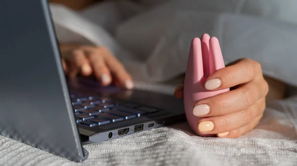 한 여성은 침대에 누워 음경 진동 장치를 들고 노트북에서 포르노를 보고 있습니다. 온라인으로 섹스하는 여자 — 스톡 사진