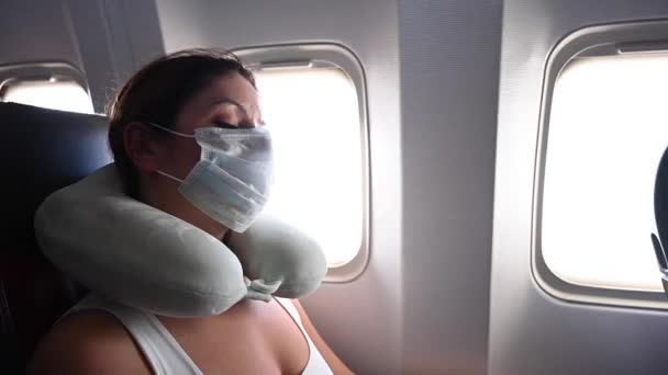 飛行中 飛行機の窓のそばに座っている間 マスクの白人女性は眠っています 枕を持つ女性 — ストック動画