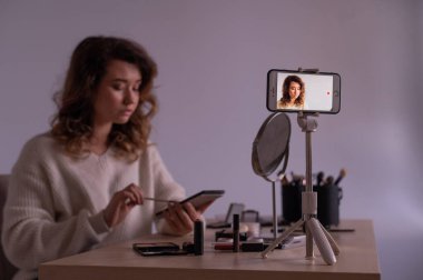 Kafkasyalı genç bir kadın cep telefonunda bir makyaj eğitimi videosu kaydediyor. Video blogcusu kız makyaj yapıyor.