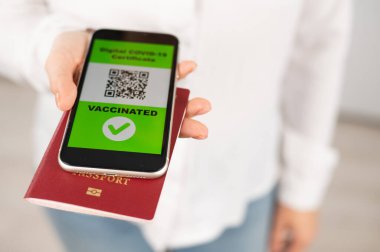 Pasaportu ve telefonu olan bir kadın aşı ile ilgili QR kodu taşıyor..