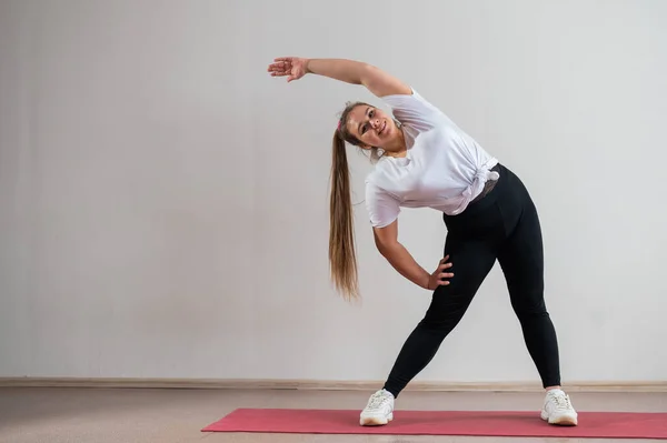 Jeune femme grosse faisant des exercices de flexibilité sur un fond blanc — Photo