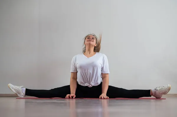 En ung flexibel fet kvinna sitter i ett tvärgående garn och viftar håret mot en vit bakgrund — Stockfoto