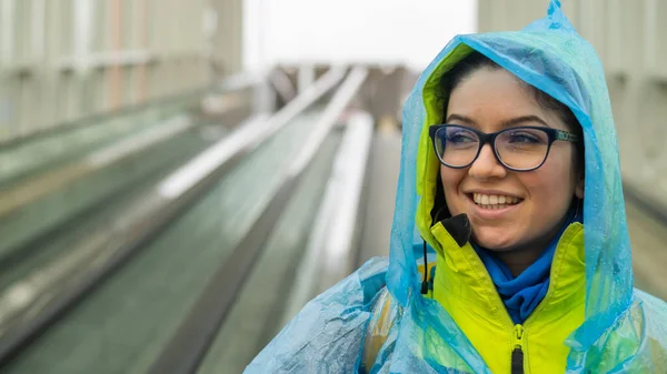 Mujer joven sonriente con chaqueta y impermeable en un travolator. Chica con ropa protectora de la lluvia —  Fotos de Stock