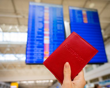Havaalanı bilgi panosunun arka planında pasaportu olan bir kadın..