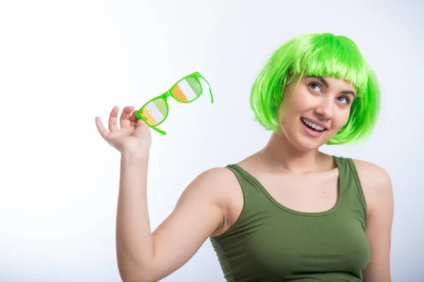 Joyeux jeune femme en perruque verte et lunettes drôles célébrant st patricks jour sur un fond blanc — Photo