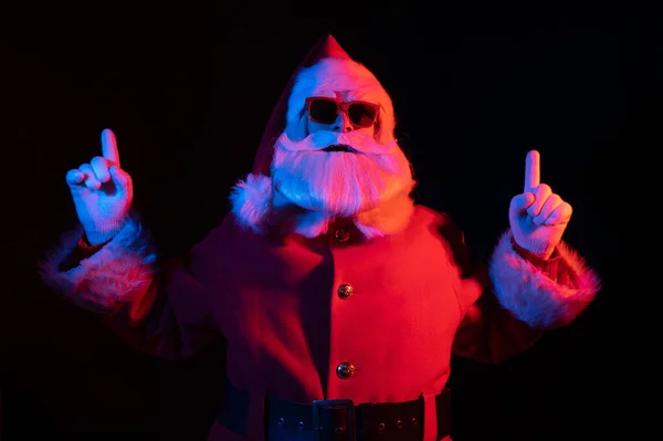 Weihnachtsmann mit Sonnenbrille in Neonlicht auf schwarzem Hintergrund. Weihnachtsfeier. — Stockfoto