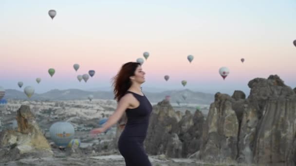 Kaukasisk kvinna som poserar mot bakgrund av ballonger som flyger över Kappadokien vid soluppgången. — Stockvideo