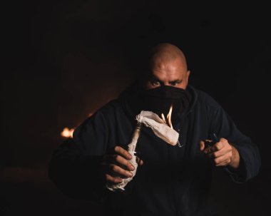 Maskeli bir adam yanan bir şişe tutuyor. Molotof kokteyli.