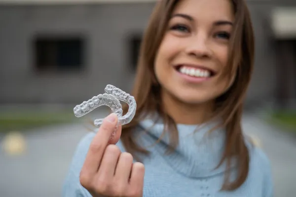 Caucasian woman with white smile holding transparent removable retainer. Bite correction device.