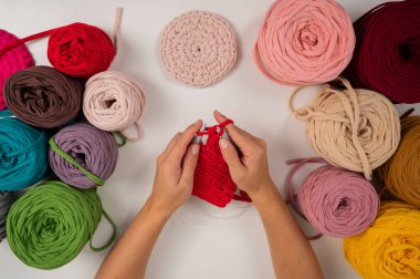 Beyaz bir masada örgü ören kadın elleri. Bir kadın bir sepet kırmızı pamuk örüyor..