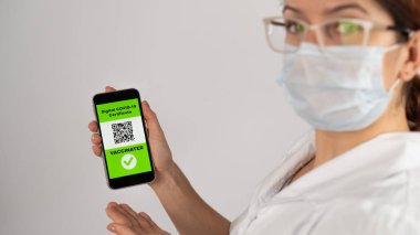 Doktor aşı öneriyor ve QR kodlu bir akıllı telefon tutuyor..