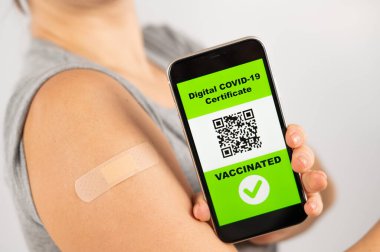 Aşıdan sonra omzunda alçı olan bir kadın akıllı telefondan QR kodunu gösteriyor..