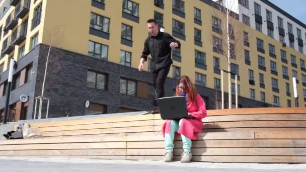 Homme caucasien faisant des sauts périlleux dans la rue et s'assoit à côté de la femme. Le gars rencontre la fille d'une manière inhabituelle. — Video