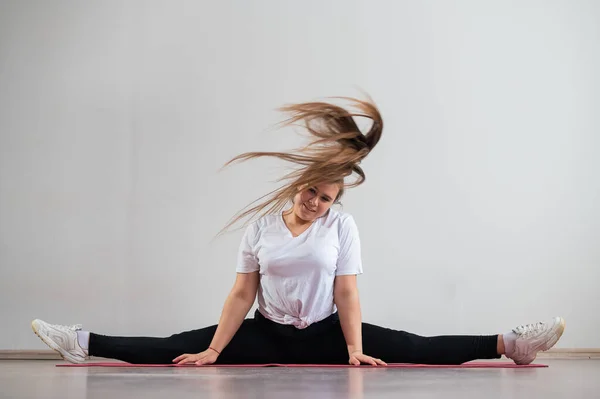 Une jeune femme grasse flexible s'assoit dans une ficelle transversale et agite ses cheveux sur un fond blanc — Photo