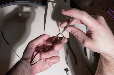 Optik teknisyen gözlükleri tamir ediyor. Tornavida ve gözlük çerçeveli erkek ellerinin yakın çekimi.