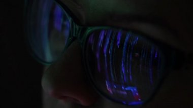 Gözlüklü beyaz bir kadının yakın plan portresi karanlıkta bir matrisle ekrana bakıyor. Ekran yansıması.