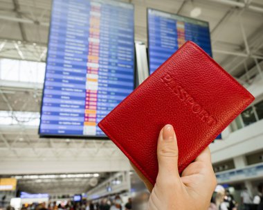 Havaalanı bilgi panosunun arka planında pasaportu olan bir kadın..