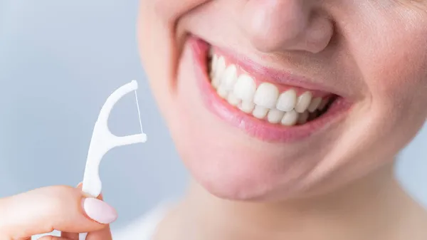 Close-up portret van een mooie blanke vrouw met een vlekkeloze glimlach met een tandenstoker met tandzijde op een witte achtergrond — Stockfoto
