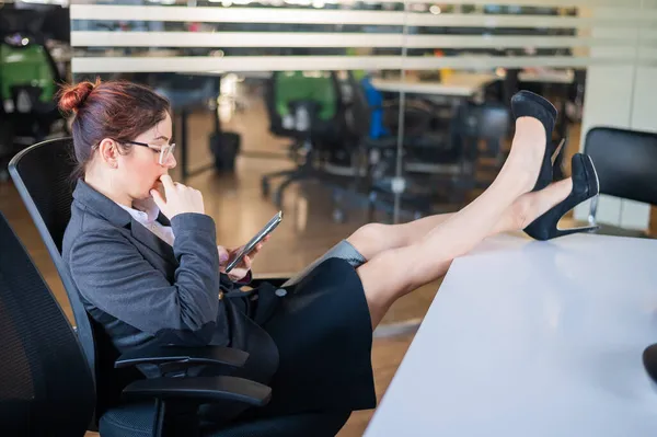 Biznes kobieta umieścić stopy na biurku i używa telefonu komórkowego w biurze — Zdjęcie stockowe