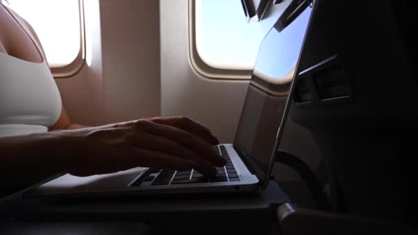 Bezimienna kobieta w masce pracuje na laptopie w samolocie siedząc przy oknie podczas lotu. Wolny strzelec w podróży. — Wideo stockowe