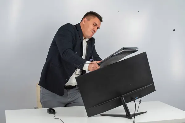 Vit man i kostym blir arg och krossar tangentbordet på skärmen. En kontorsanställd i ilska knäcker datorn. — Stockfoto