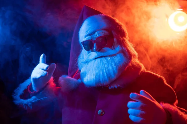 Santa Claus en gafas de sol en humo rojo-azul. Fiesta de Navidad. — Foto de Stock