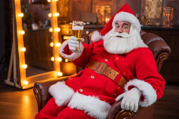 Ο Άγιος Βασίλης πίνει μπύρα ενώ κάθεται σε μια δερμάτινη πολυθρόνα — Φωτογραφία Αρχείου